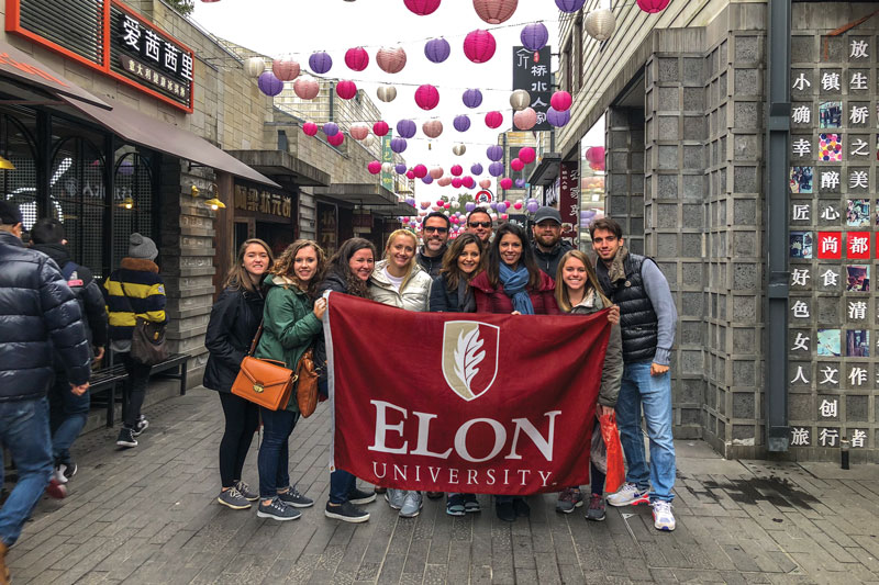 A group of students with a professor holding an Elon University banner.