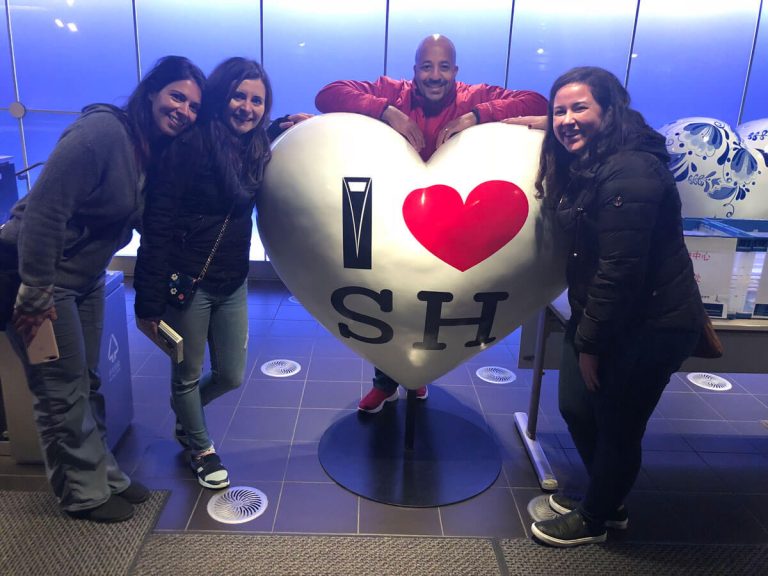 four elon MBA program students in front of a sculpture that reads I heart shape S H