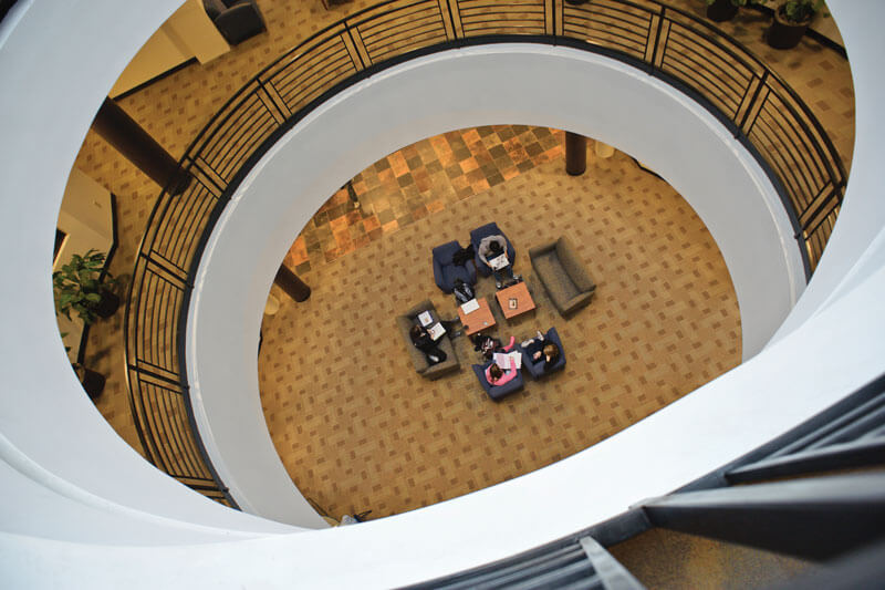 A view from an upper floor of a building looking down on a lounge area with several tables and chairs.