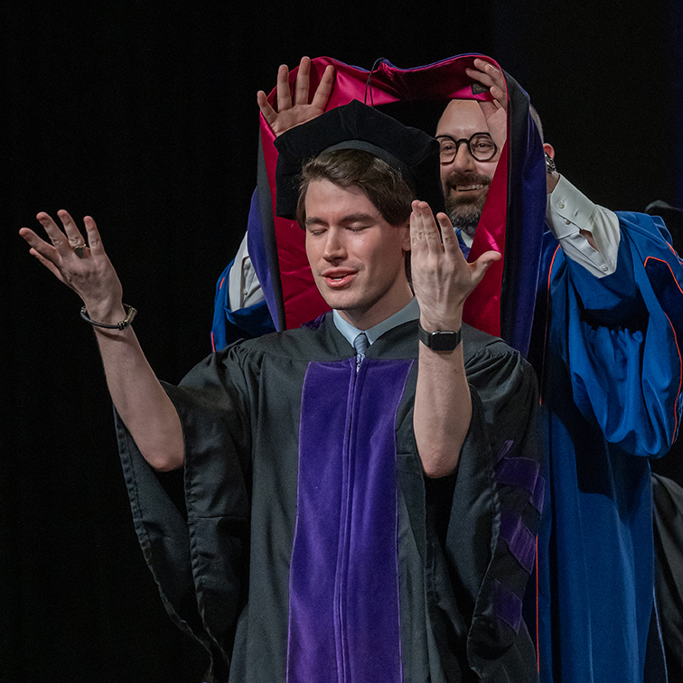 A dean places a stole around the neck of a graduating male law student.