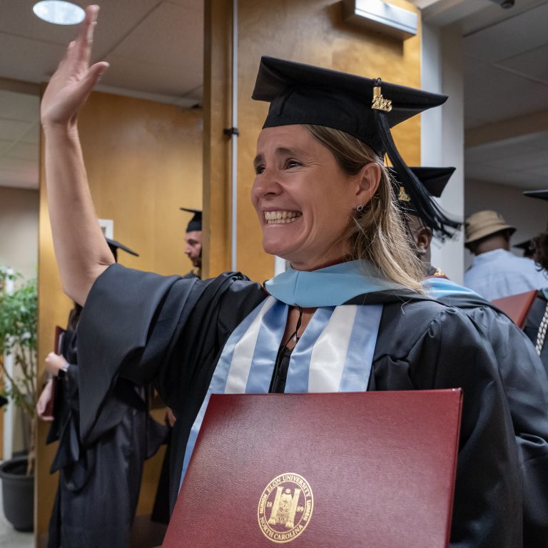 A master's-level graduate holding her diploma and waving