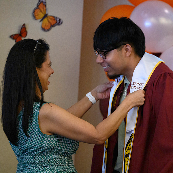 A female staff member places a white stole around the neck of a male graduate