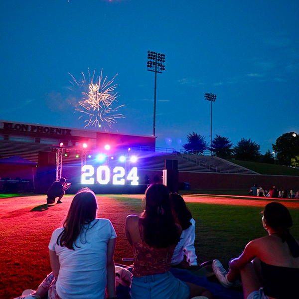 A group of female students watch fireworks above a lighted 2024 sign