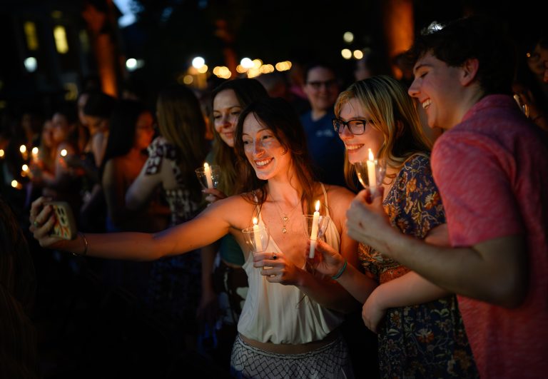 Students holding candles gather for a selfie during Elon University’s Senior Baccalaureate celebration.