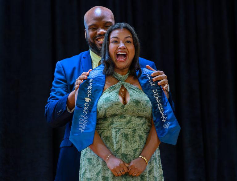A student reacts with excitement as a blue first-generation stole is placed around her shoulders during Elon University’s First-Generation Stole Ceremony.