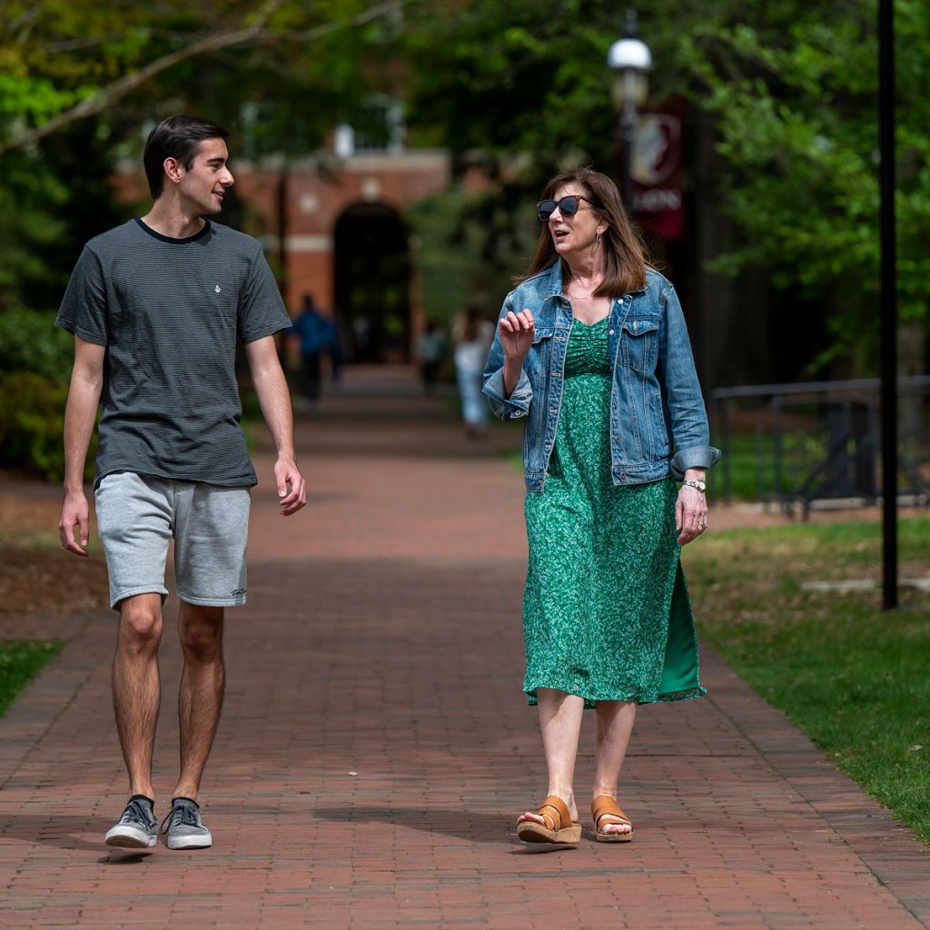 Cole Carney and his mentor, Cindy Fair, walking downa brick pathway with a brick arch in the background.