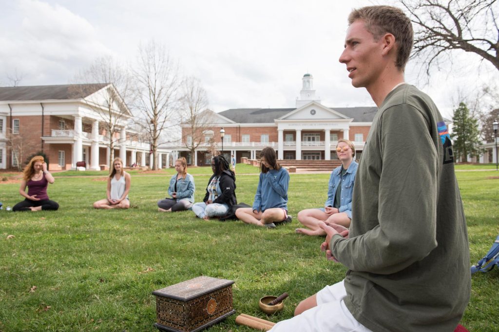 A group of individuals sitting on grass in meditation poses.