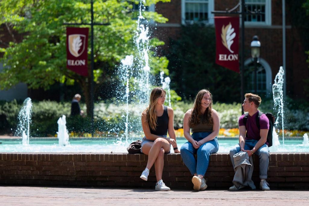 Three people sitting on the edge of a brick fountain and having a conversation.