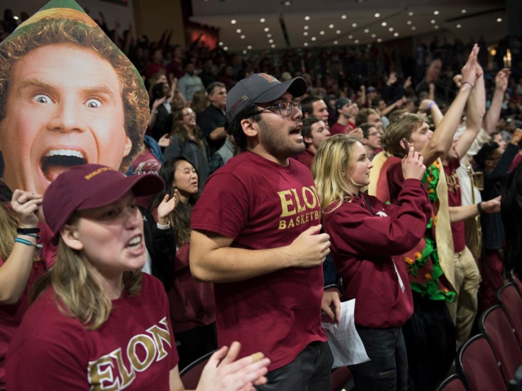 Large crowd of people dressed in maroon and gold cheering at a basketball game.