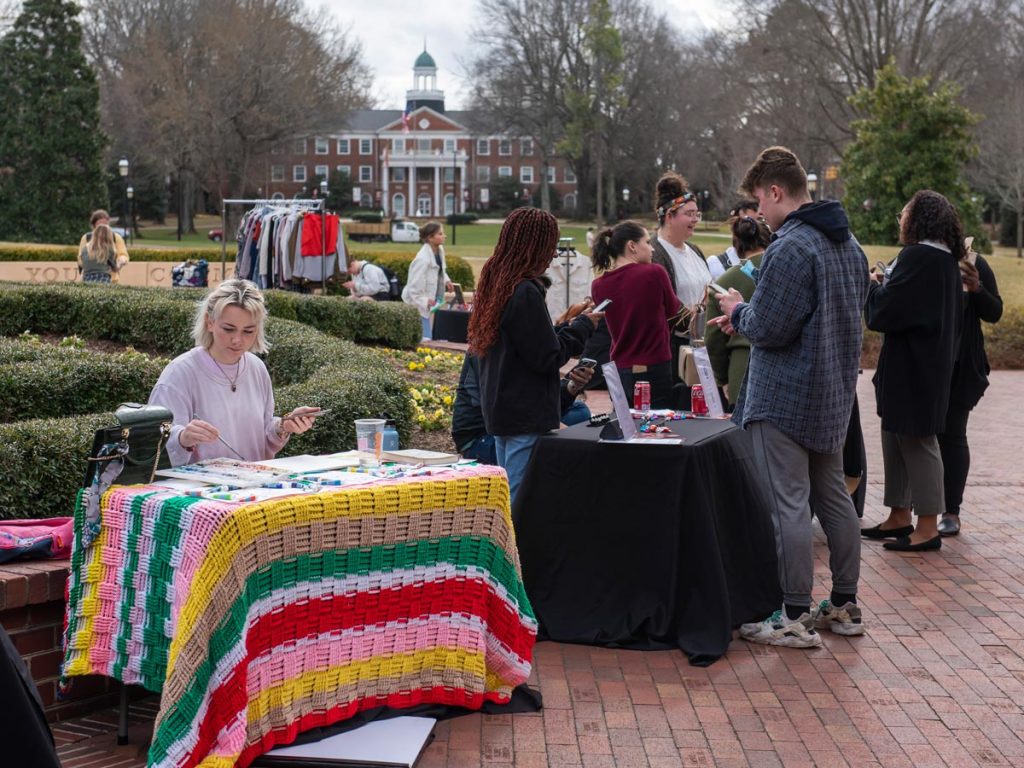 An Elon student paints at a table for their business at the Marketplace Under the Oaks Pop-Up Shops.