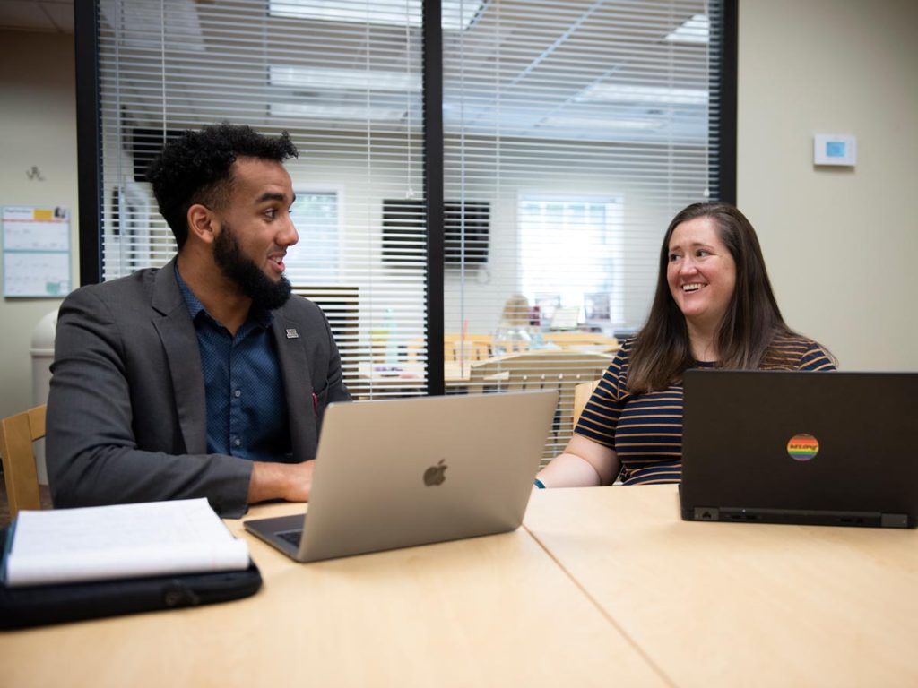 An Elon Center for Leadership staff member and her apprentice sitting at a table in a conference room working with laptops in front of them.