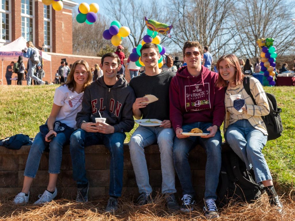 Five people sitting on a stone wall posing for a photo during an Elon Day celebration.