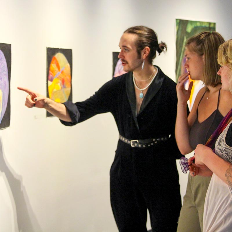 A person pointing to a piece of art on a gallery wall as two other individuals stand behind them.