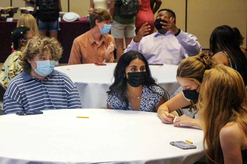 Groups of masked students sitting around round tables.