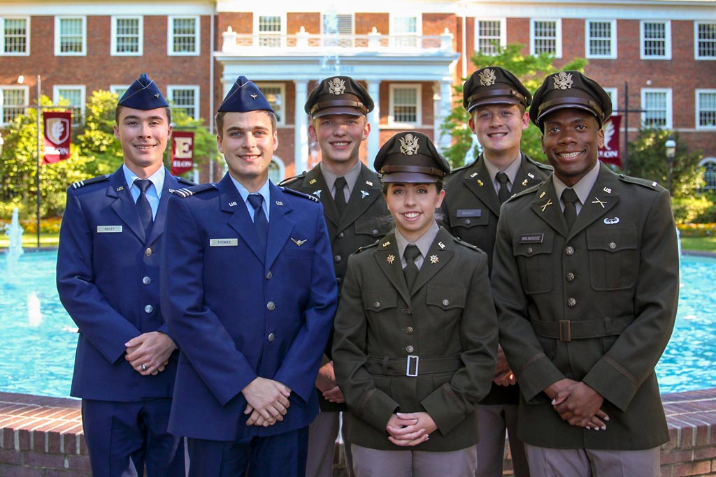 A group of six ROTC students posing in front of a brick building and fountain on Elon's campus.