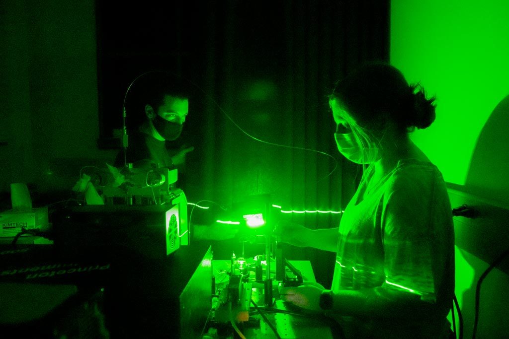 Elon student Anna Sheinberg in a lab glowing with a green hue as she uses lasers to analyze aqueous carbonic acid.