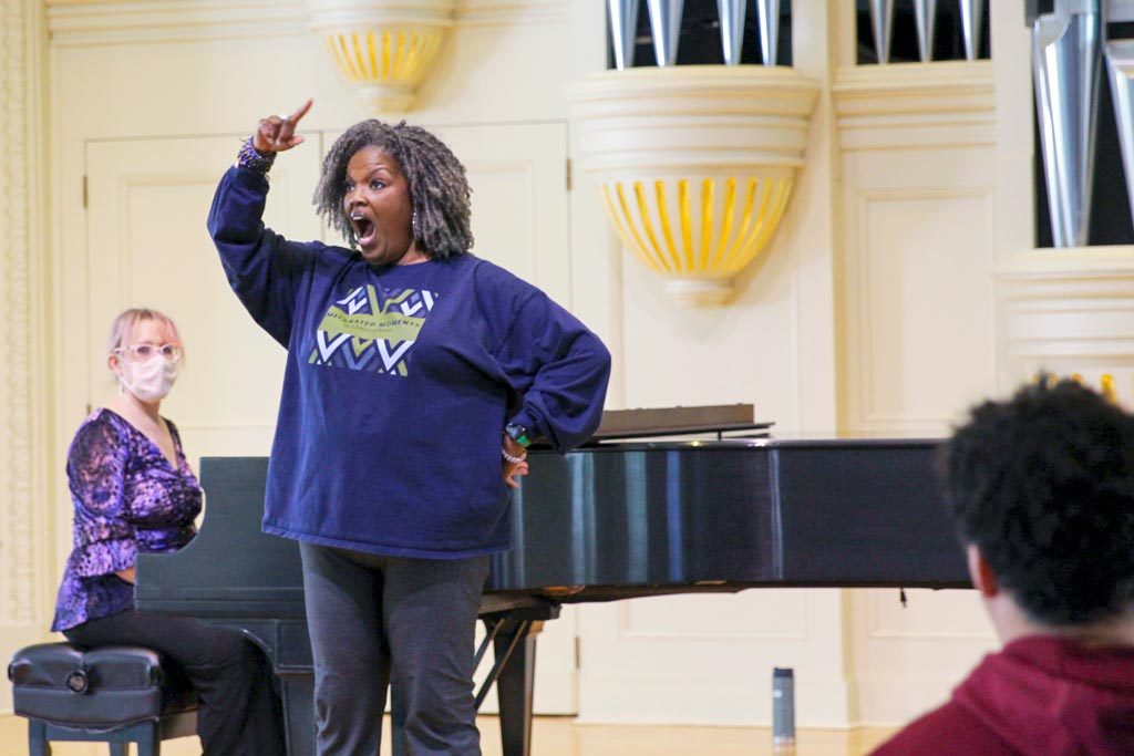 Opera singer Angela Brown singing on stage in front of a piano during a master class for music and arts administration students.