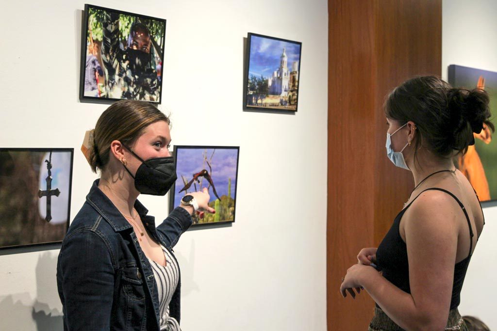 A student points to a piece of artwork displayed on a wall for Elon's Borderlands exhibit.