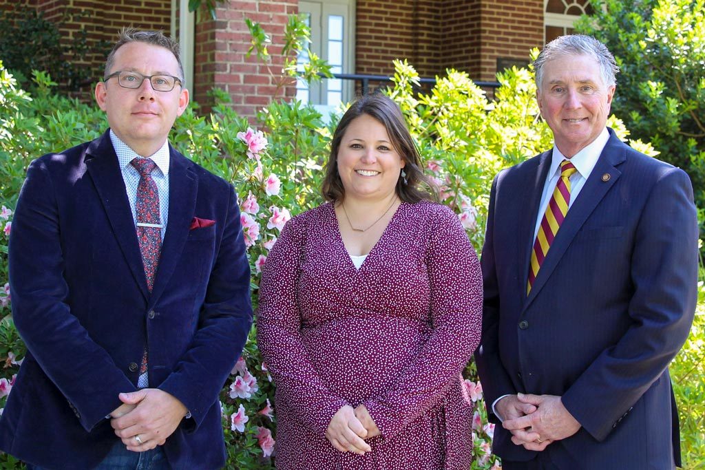 Elon alumni Kevin Pace, Sarah Babcock and Drew Van Horn pose for a group photo in front of a flowering bush.