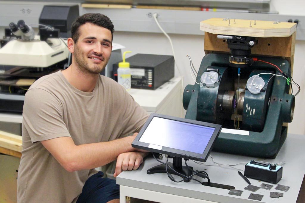 Elon student Stratton Bacogeorge kneels beside the magnetometer device he built.