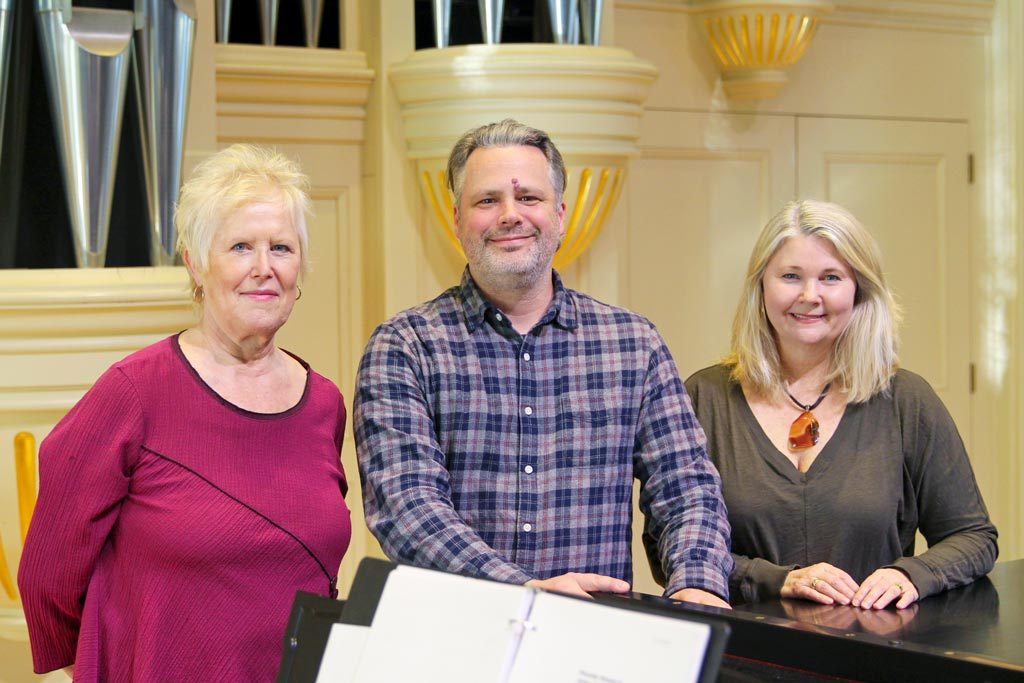 Chris Miller standing behind a piano in Elon's Whitley Auditorium with two music faculty members.