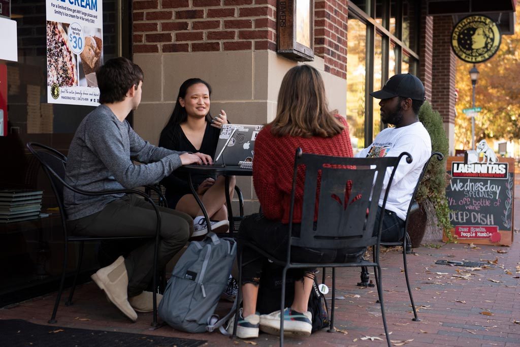 Four students sitting at a table outside of downtown Elon's Pandora's Pies restaurant.