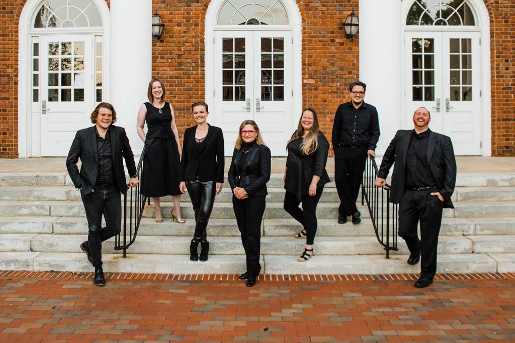 Seven members of the Elon Contemporary Chamber Ensemble pose for a photo on the steps in front of a brick building.