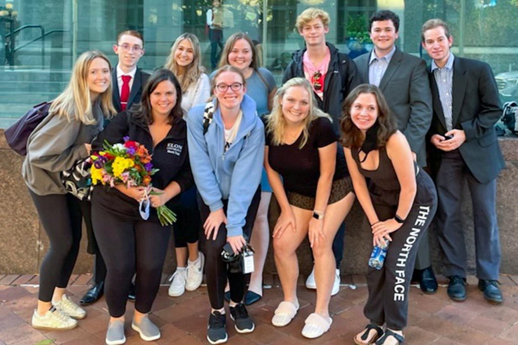 The Elon mock trial team poses for a photo on a walkway in front of a building with large glass windows.