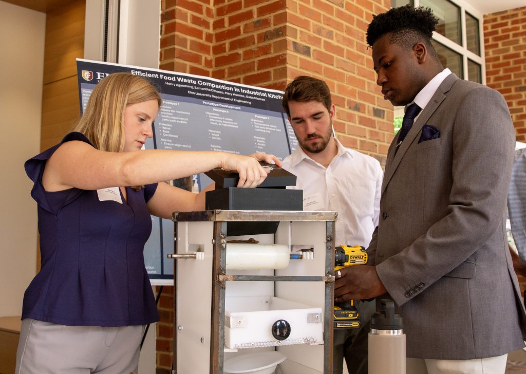 Three students test a design prototype in front of Founders Hall