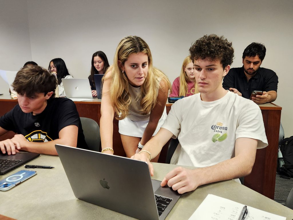 a learning assistant works with a student at his computer in a classroom