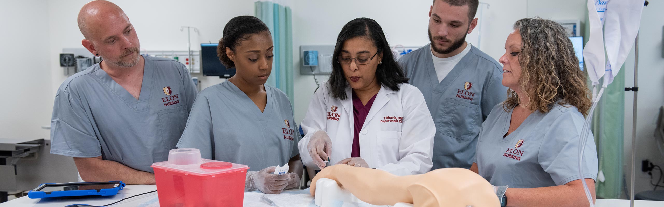 A professor showing four nursing students how to perform a medical procedure.