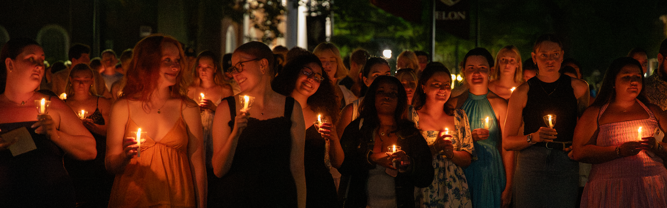 A group of Elon University students participate in a candlelight ceremony during Baccalaureate, creating a warm and reflective atmosphere under the night sky.