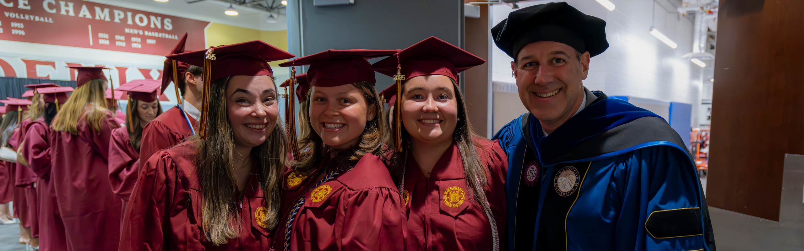 Vice President for Student Life Jon Dooley poses with three graduates in maroon caps and gowns before the start of Elon University's commencement ceremony.