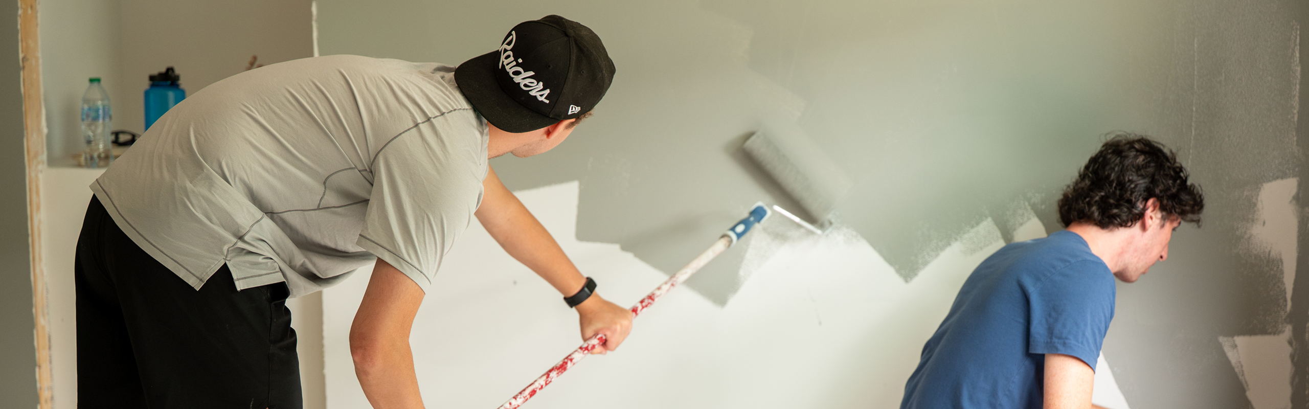Two Elon University students work together painting a wall during a Habitat for Humanity service project.