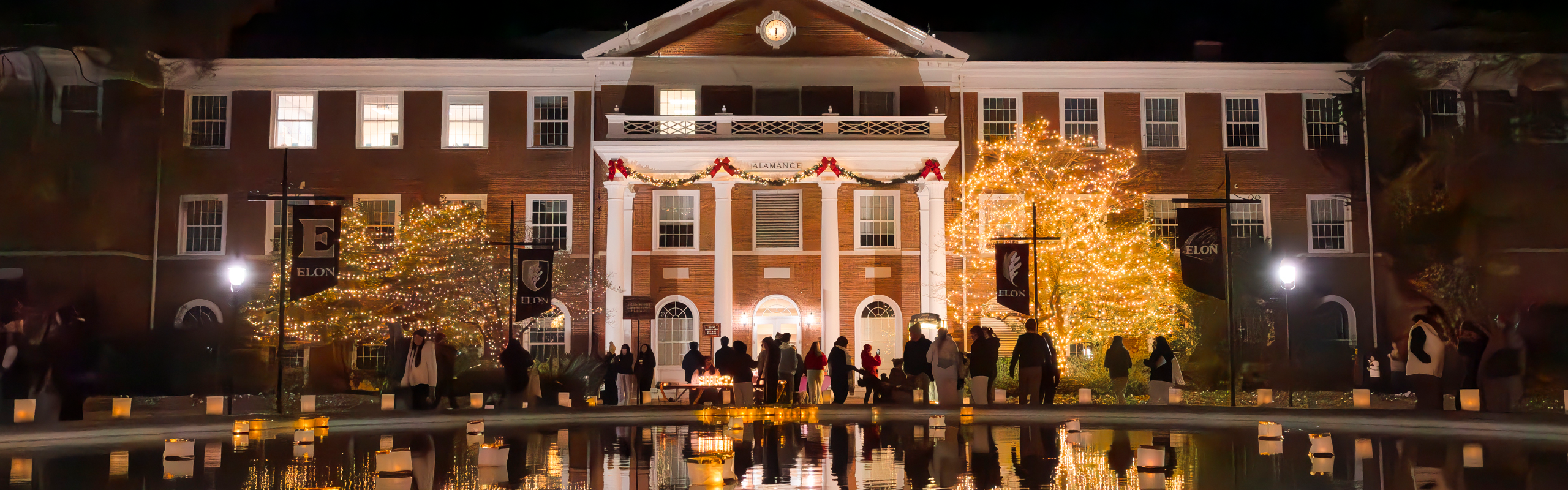 People gather in front of Elon University's Alamance Building decorated with holiday lights and luminaries during the annual Lights and Luminaries celebration.