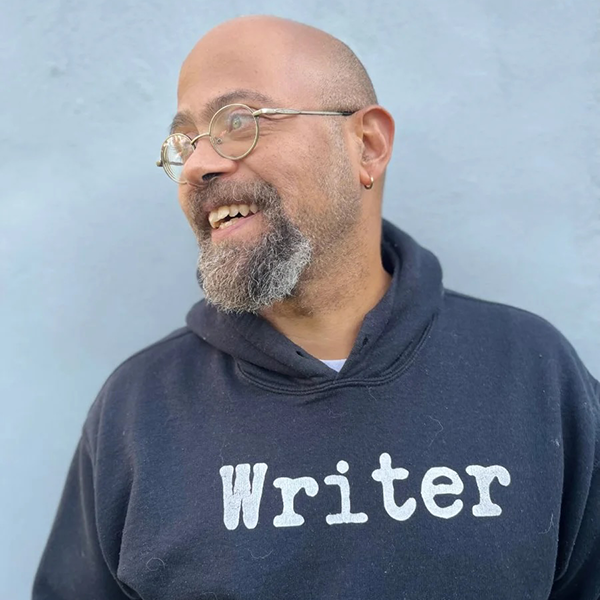 A man wearing a sweatshirt with the word "writer" on the front looking away from the camera and smiling