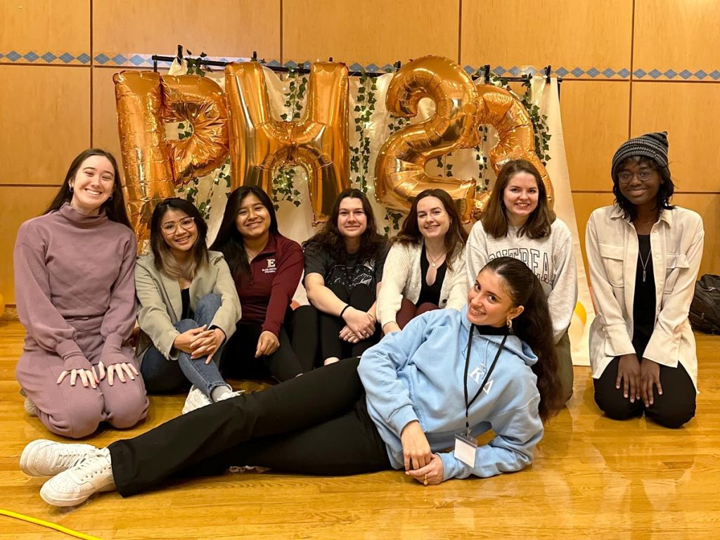 Elon Women in STEM members gather around oversized balloons shaped as the letters 'P' and 'H' along with the numbers '2' and '3'.