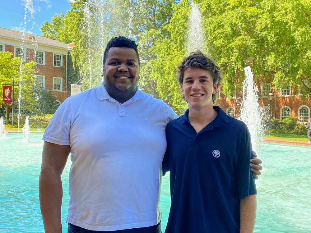 Nicholas Rugbart and Bo Dalrymple stand together beside Fonville Fountain on Elon University's campus.