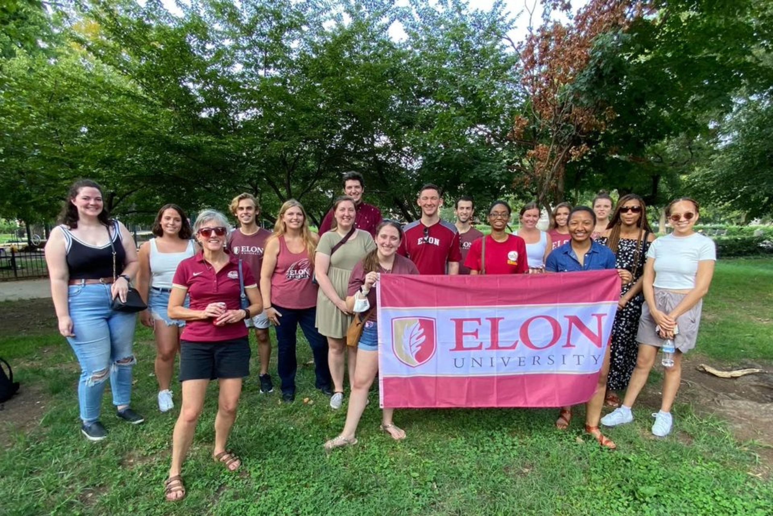 students and staff holding elon university flag in park