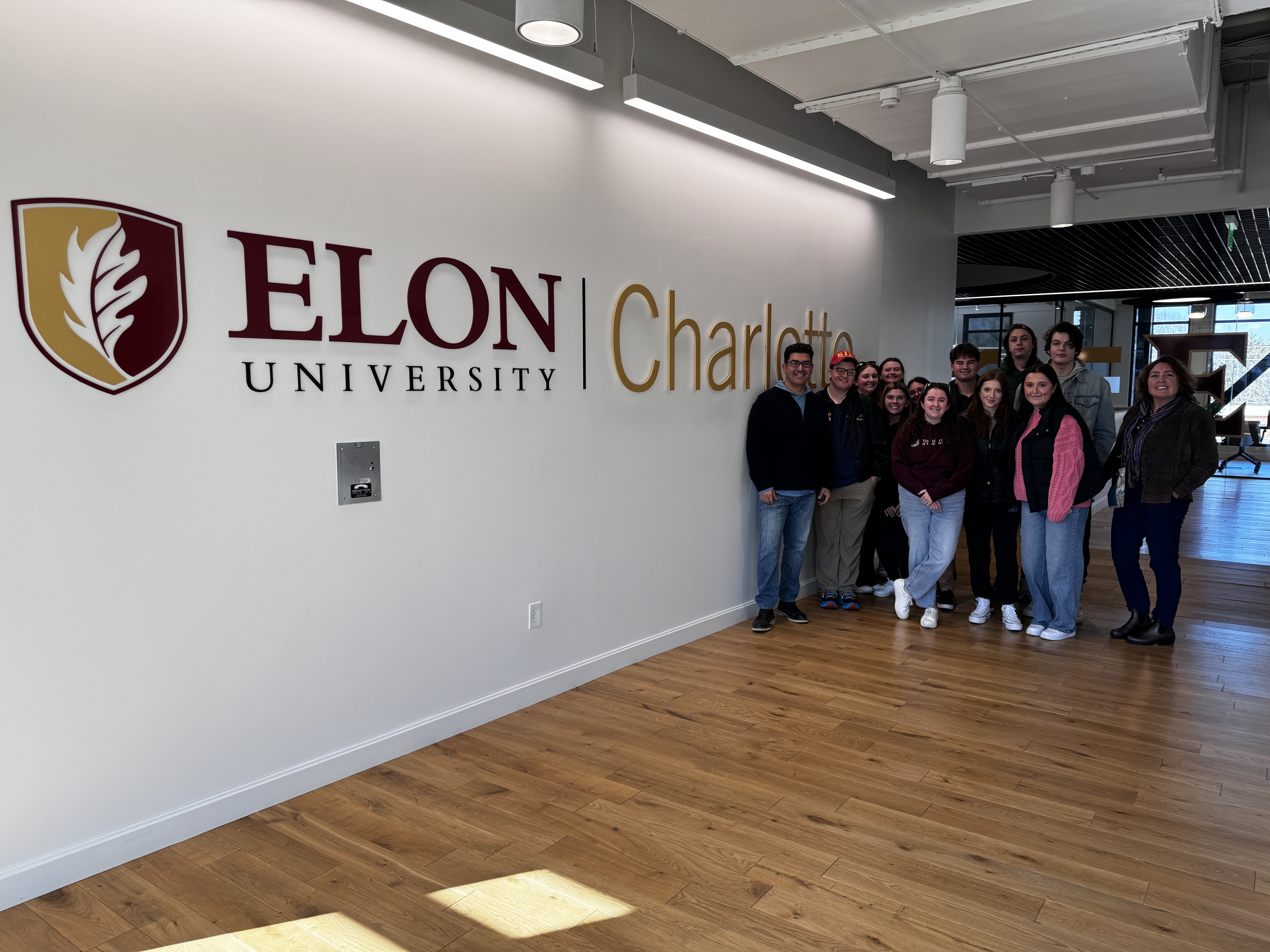 A group of students standing next to Elon in charlotte sign on wall