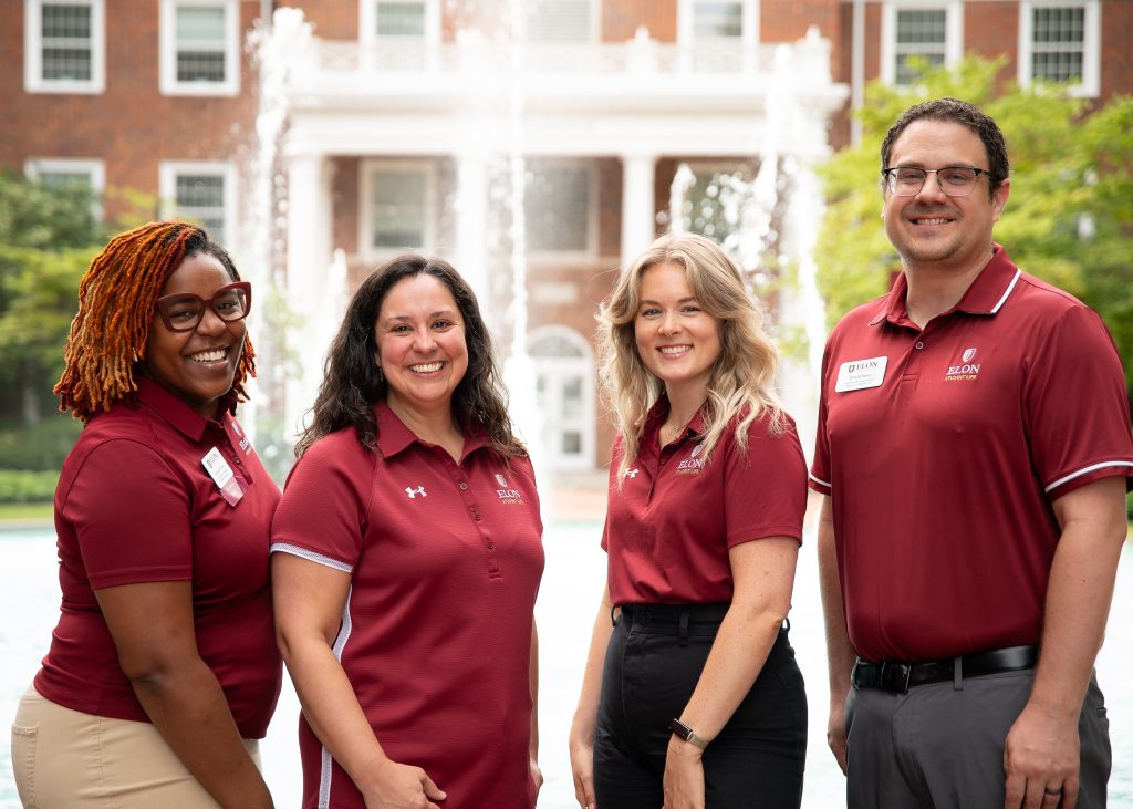 Four smiling staff members pose with the fountain in front of the Alamance building