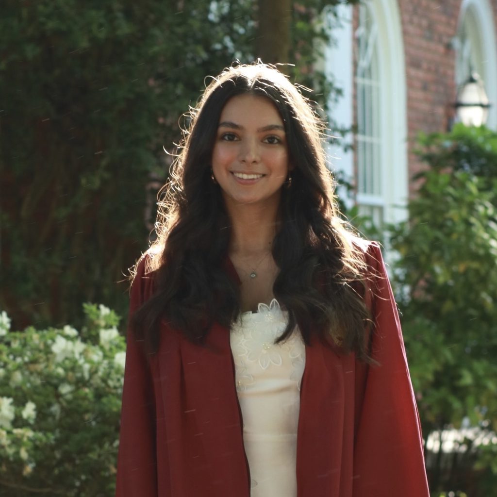 a woman in a maroon graduation gown smiles at the camera