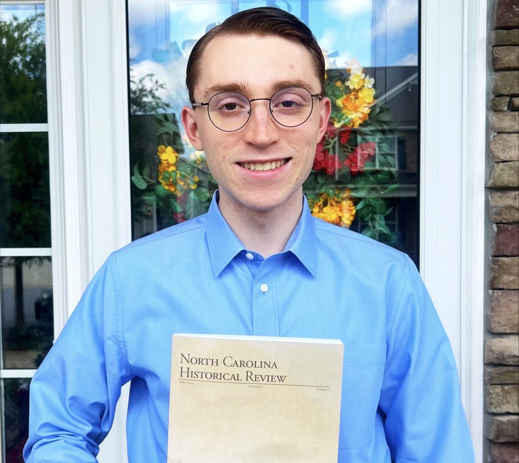 a man wearing glasses and a blue collared shirt holds an academic journal North Carolina Historical Review