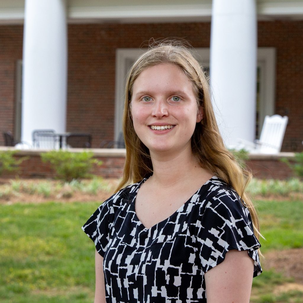 A female student in a black and white blouse in front of academic buildings with white columns