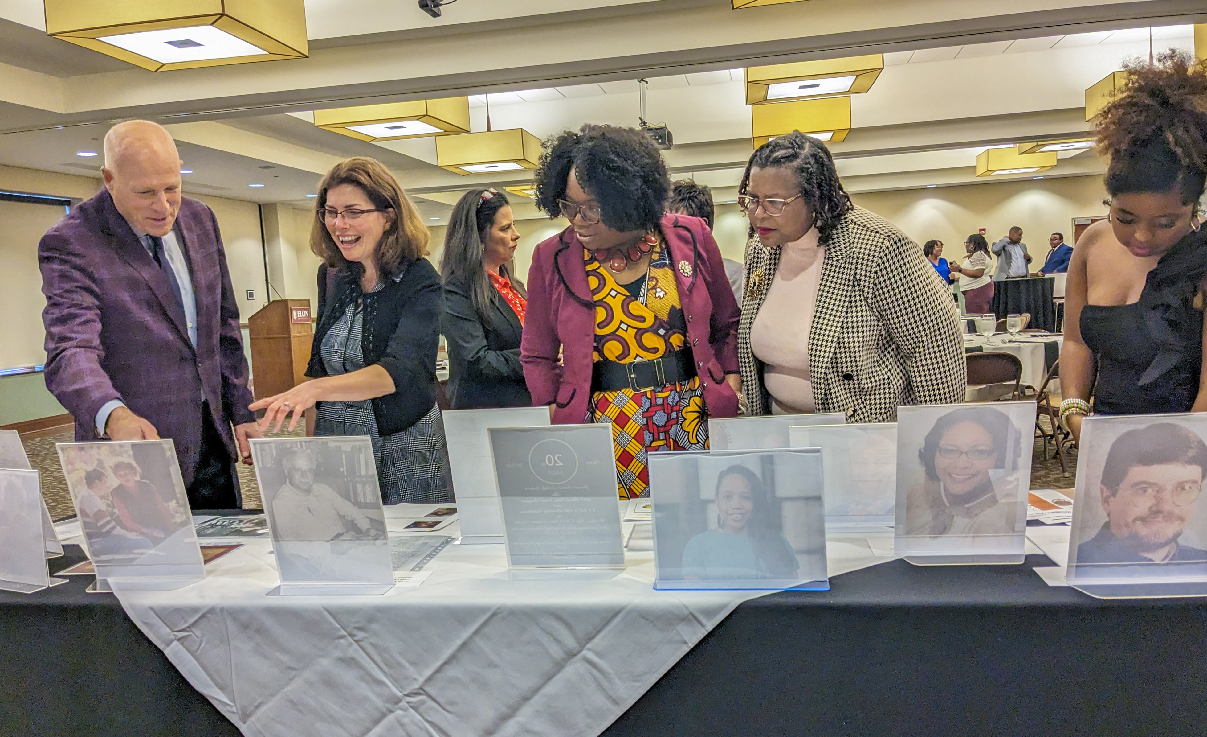 photo shows people behind a display table pointing to photos and reading information