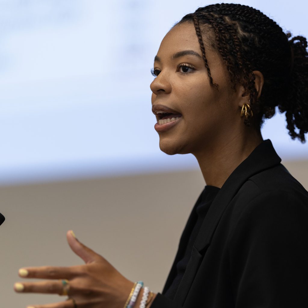 a female student gives a presentation. she is shown speaking and gesturing with her hands
