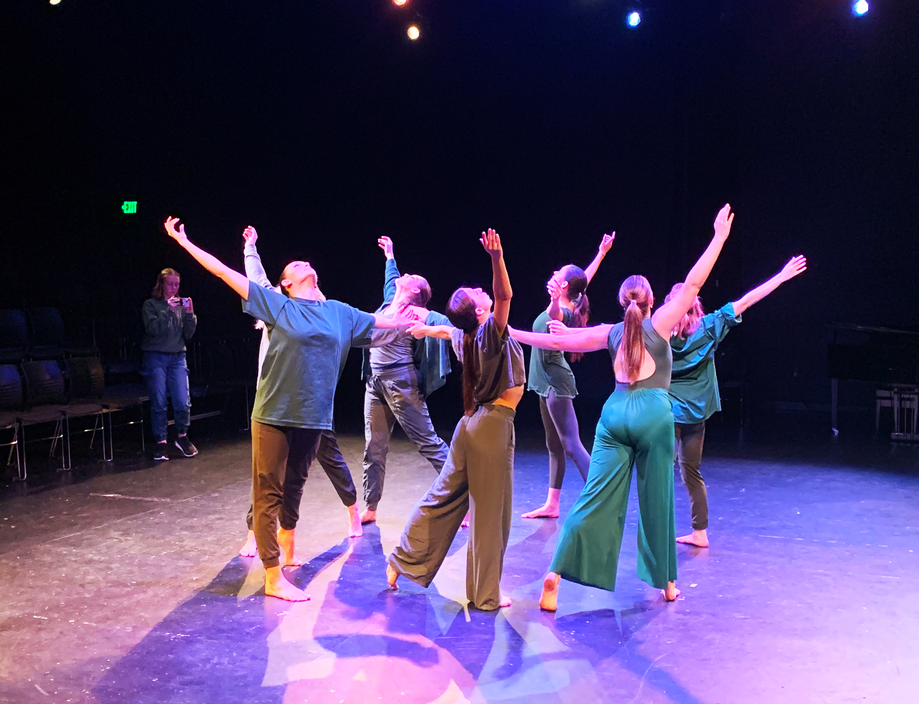 a group of dancers onstage in a circle formation raise their arms and point upward