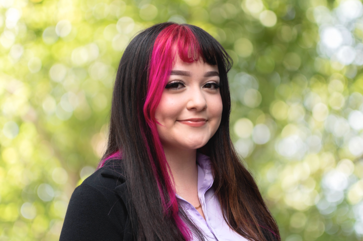 Tyra Duque, with black and pink hair, smiles at the camera on Elon University's campus