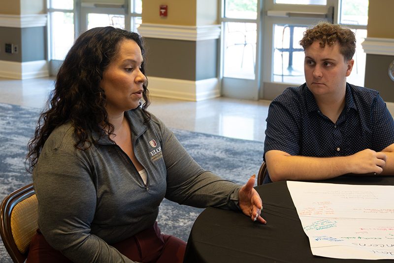 ������Ƶ MHE program orientation photo of faculty and student discussing at a table