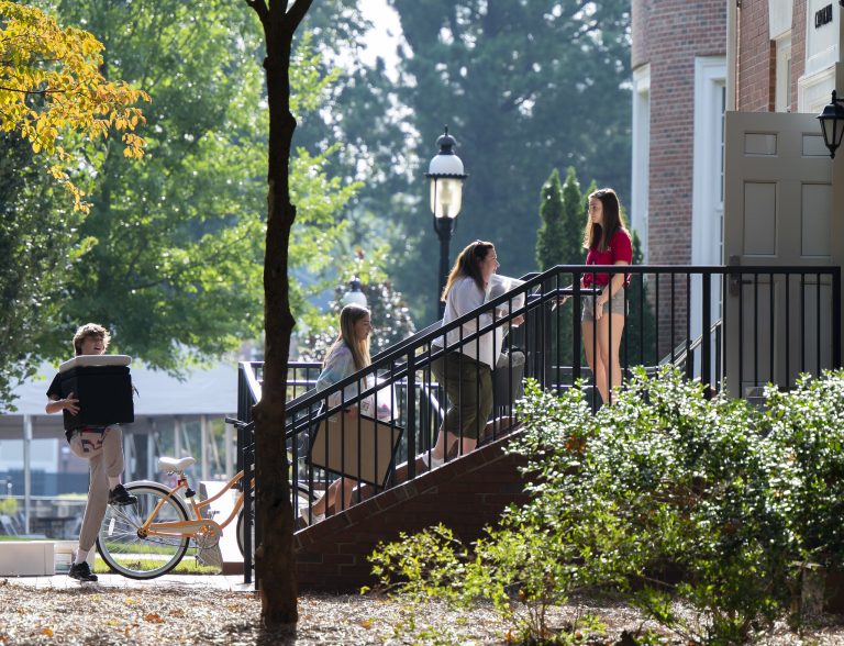 Students carry boxes and belongings up the steps of a residence hall during move-in day on campus.